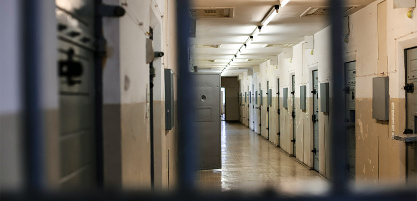Durch eine Gittertür schaut man in den langen Gang eines in die Jahre gekommenen Gefängnisses.