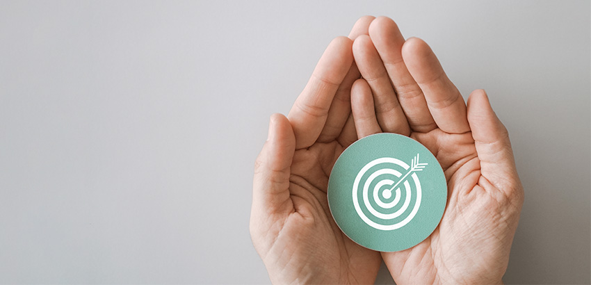 Zwei Hände halten einen Kreis, auf dem eine Zielschreibe mit einem Pfeil abgebildet ist.