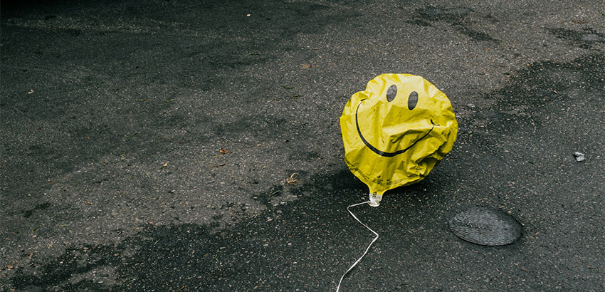 Ein goldener Ballon mit einem lachenden Smiley-Gesicht, liegt leicht zerknittert auf der Straße. 