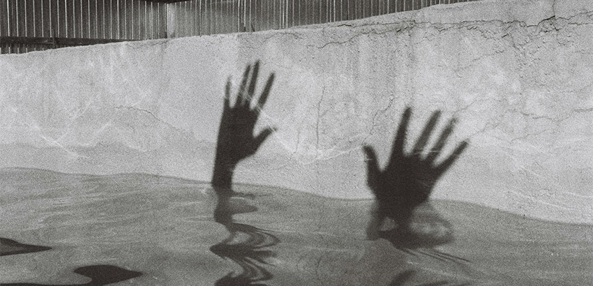 Die Schatten zweier nach oben gestreckter Hände an der Seitenwand eines Schwimmbeckens.