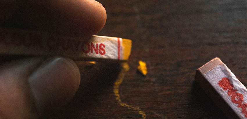 Eine Hand, die eine sehr kurvige Linie mit einer Pastellkreide zeichnet.
