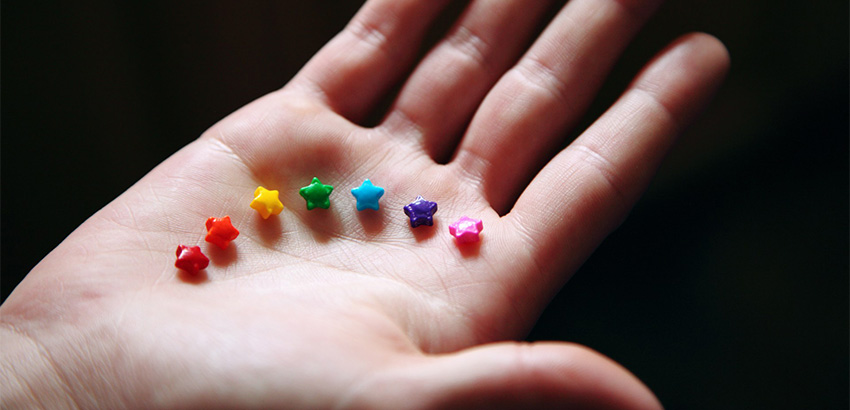Auf einer Hand liegen sternenförmige Perlen in Regenbogenfarben.